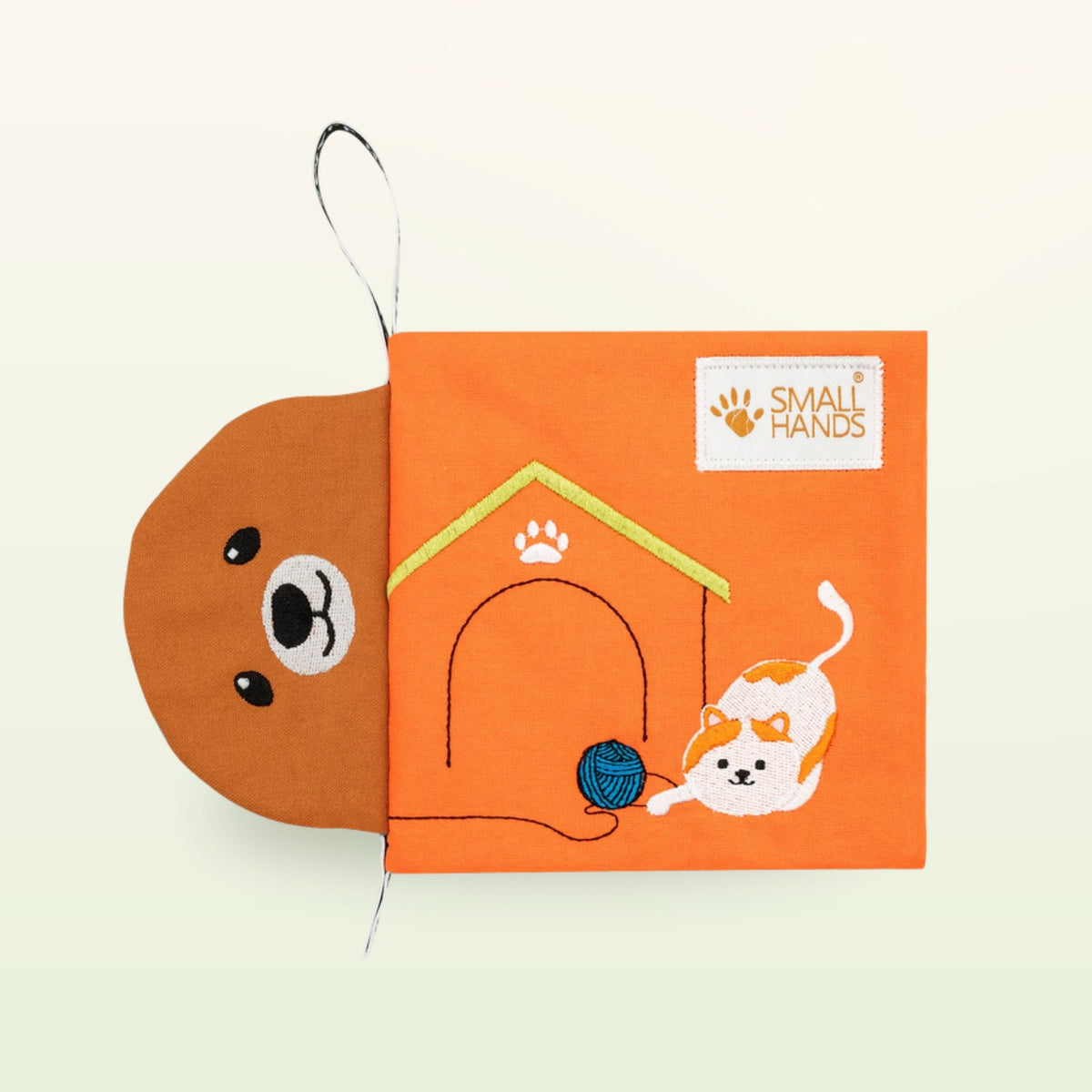 Small Hands Mascotas libro de tela Montessori – cubierta naranja con cara de perro, caseta y gato jugando sobre fondo suave de color crema – a partir de 0 meses