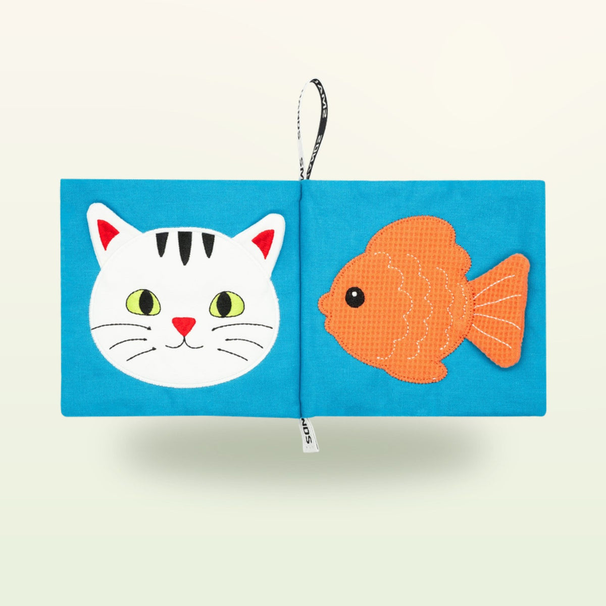 Small Hands Mascotas libro de tela Montessori abierto – cara de gato y pez dorado sobre fondo suave de color crema – a partir de 0 meses