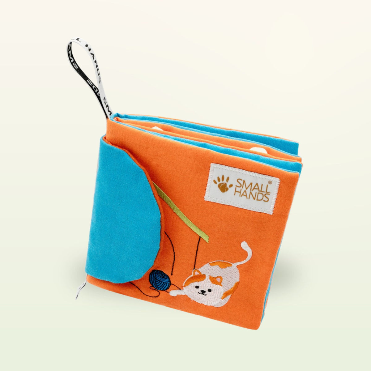 Small Hands Mascotas libro de tela Montessori en vista oblicua con páginas de tela apiladas y gato sobre fondo suave de color crema – a partir de 0 meses