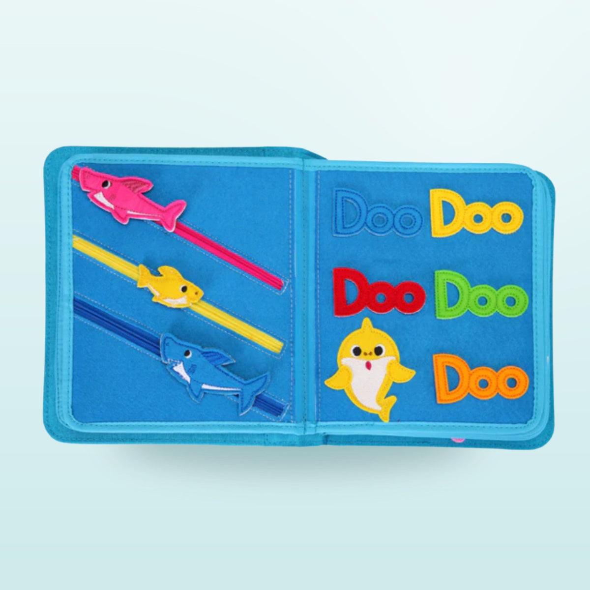 Doble página del quiet book Baby Shark con tiburones deslizables y letras Doo-Doo-Doo de colores sobre fondo suave de mar – colores y motricidad fina a partir de 3 años